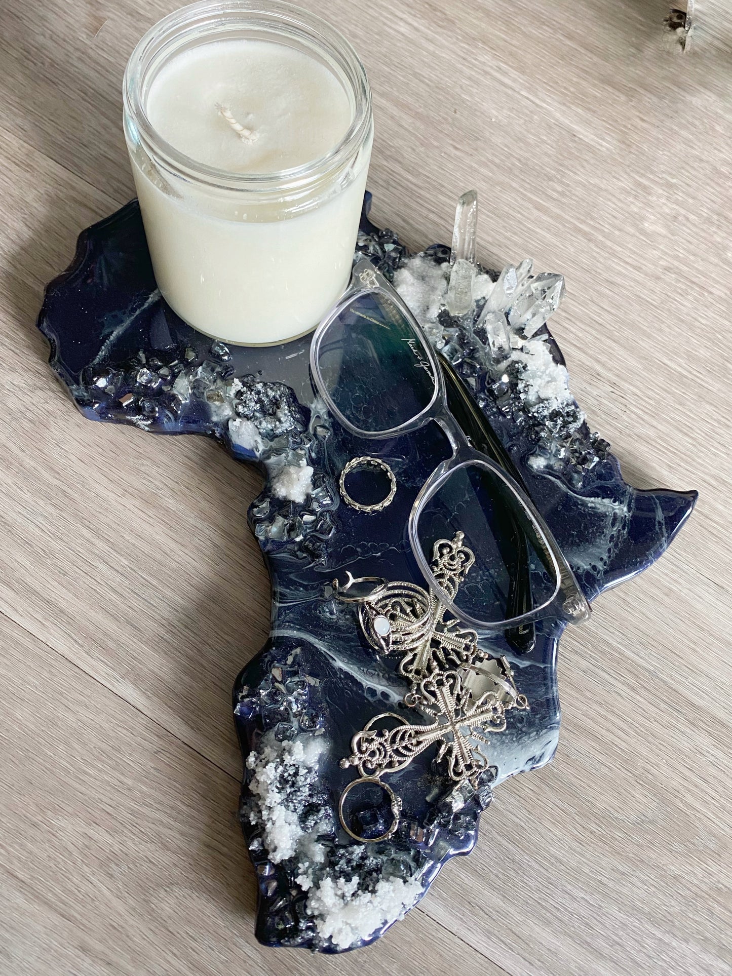 Functional art Africa shaped tray for use with jewelry, candles, glasses or as decorative table art. Bamboo cutting board base and epoxy resin coated in navy blue with white waves. The sides are adorned with white sand, crushed glass mirror and resin crystals.