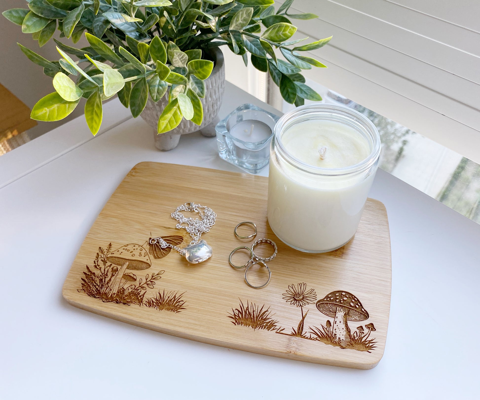 Mushroom village engraved candle tray made from mini bamboo cutting board. Sealed for protection of the wood and added rubber feet. The design has two sets of mushrooms surrounded by small flowers and leaves. Customized name or date can be added