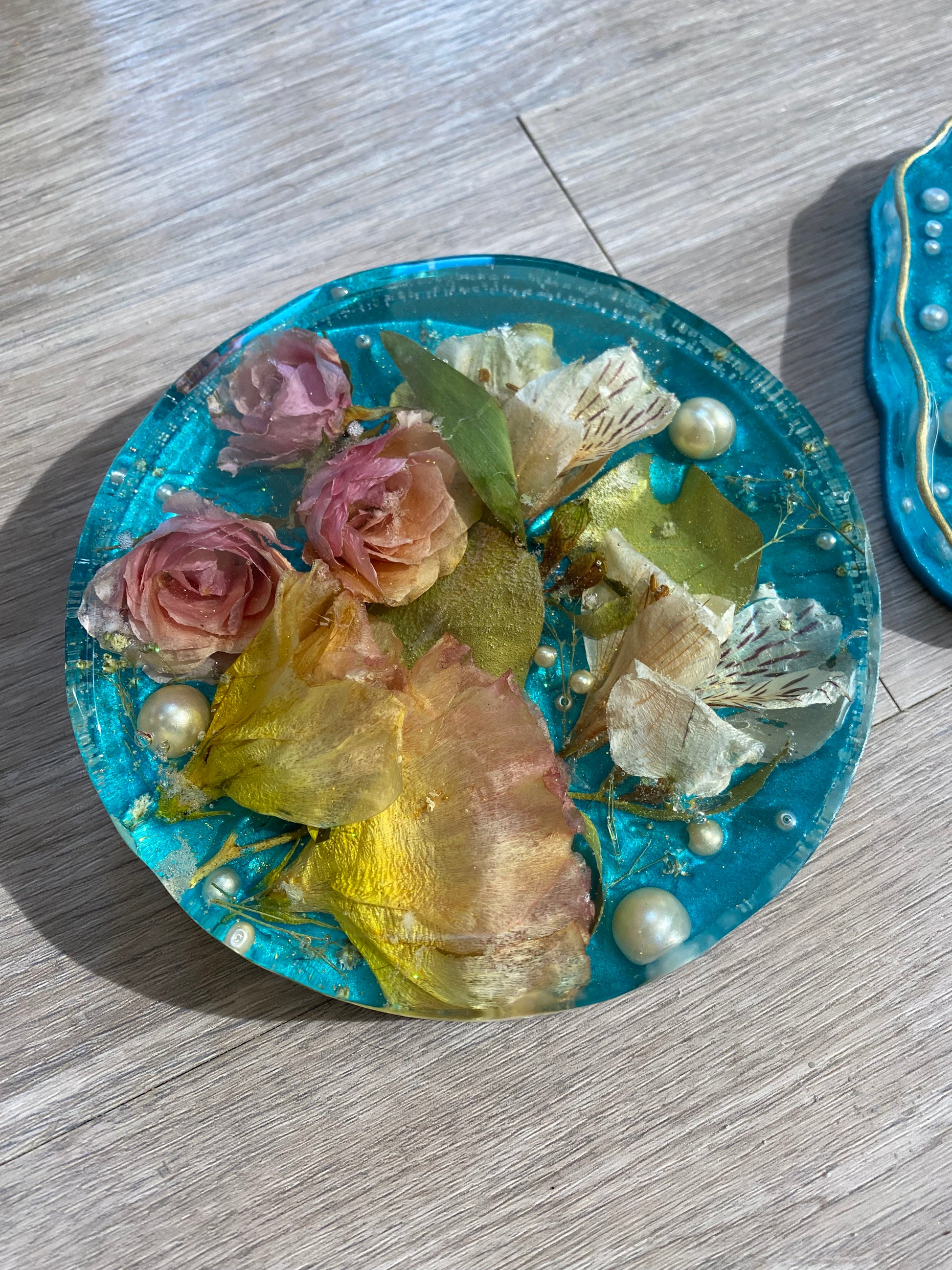 Under the Sea style flowers preserved in epoxy resin. Teal base with flowers including mini roses preserved in clear epoxy resin with round plastic pearls.